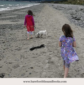 Two Girls walking on a beach with their dog
