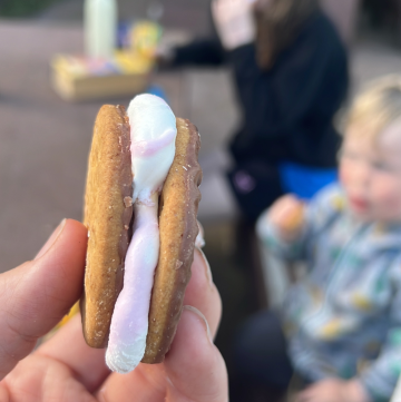 holding up a s'more made with marshmallows and chocolate biscuits